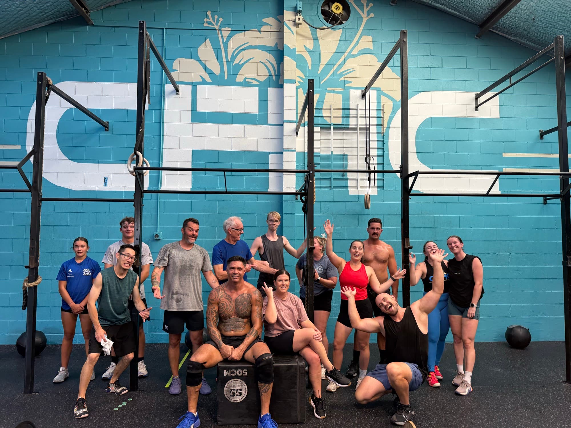 CrossFit Hibiscus Coast members gathered together in front of the gym mural wall